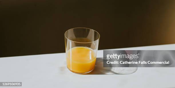 single glass of orange juice casting a shadow on a white surface with space for copy - orange juice stock-fotos und bilder