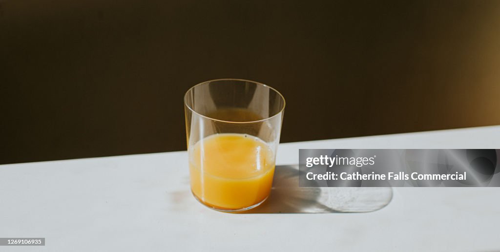Single Glass of Orange Juice casting a shadow on a white surface with space for copy