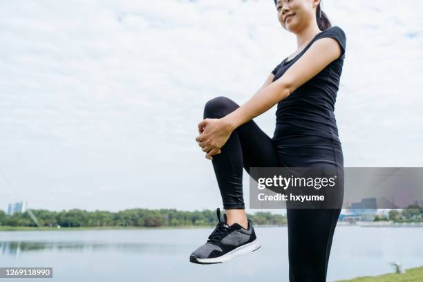 energetic asian chinese woman doing warm up exercise and streching her arm at scenic park in the morning - knee stock pictures, royalty-free photos & images