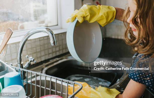 cute little girl wearing yellow washing up gloves and washing the dishes - pocket money stock pictures, royalty-free photos & images