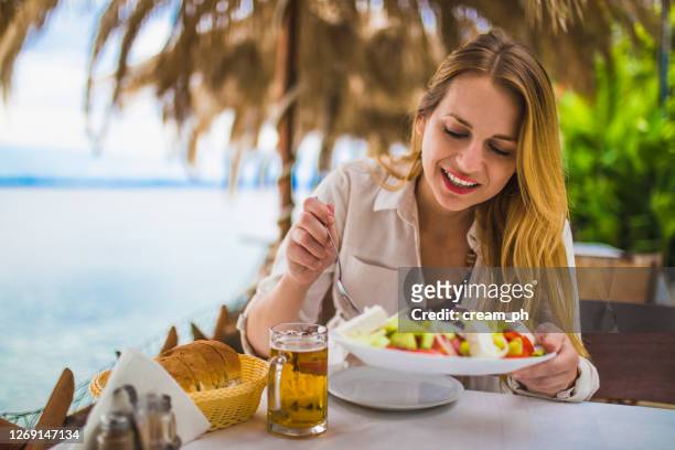 woman eating greek salad in an outdoor restaurant at the seaside - greek food imagens e fotografias de stock
