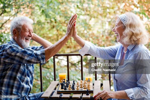 senior-paar spielt schach zu hause auf einer terrasse - alter mann jung geblieben stock-fotos und bilder