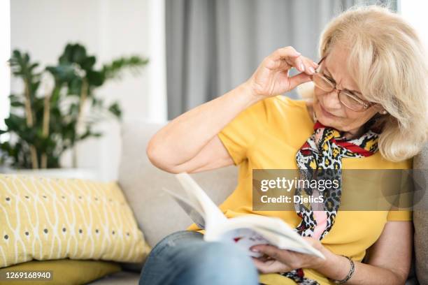 mature woman having eyesight problems reading a book. - eye problems stock pictures, royalty-free photos & images