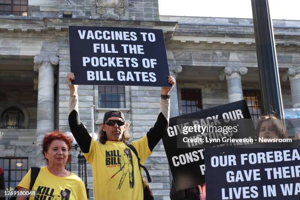 Protestors at a rally at New Zealand's Parliament on 6 August 2020 hold up posters against the rollout of 5G and vaccination, wearing T-shirt reading...