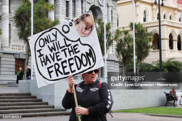 Woman holds a banner showing New Zealand Prime Minister Jacinda Ardern with a swastika on her forehead and the letters CCP on her cheek and the words...