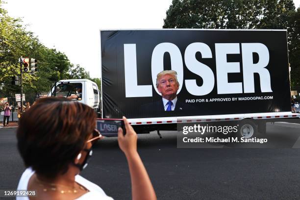 Joy Jackson photographs a passing truck bearing an image of U.S. President Donald Trump in front of block letters reading "LOSER" at Black Lives...