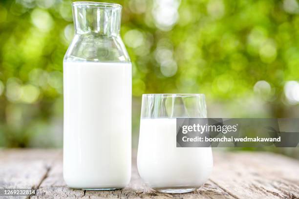 a carafe of fresh cow's milk stands on a wooden table next to a skakan, on a natural green background - milchkrug stock-fotos und bilder