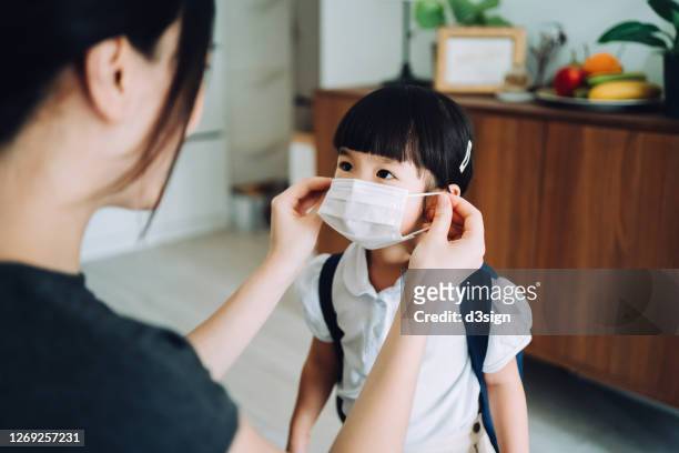 young asian mother preparing for her little daughter's first day of school and putting on a protective face mask on her daughter's face to protect and prevent from the spread of viruses - get dressed male stock-fotos und bilder