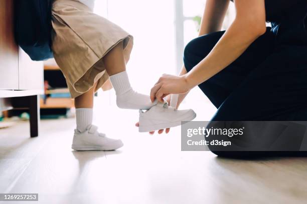 close up of young asian mother putting on shoes for her little daughter in the living room and preparing for her first day at school - school close up stock-fotos und bilder