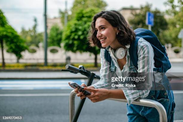 jonge vrouw met elektrische scooter op de straat gebruikend slimme telefoon - step stockfoto's en -beelden