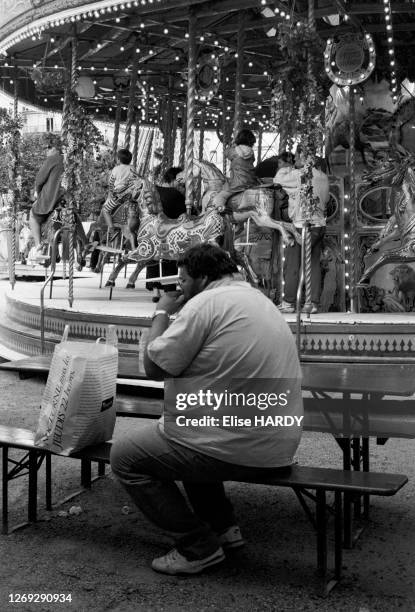 Homme obèse mangeant devant le manège du jardin des Tuileries à Paris, le 5 juillet 1992, France.