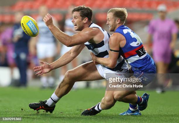 Tom Hawkins of the Cats handballs whilst being tackled by Will Hayes of the Bulldogs during the round 14 AFL match between the Western Bulldogs and...