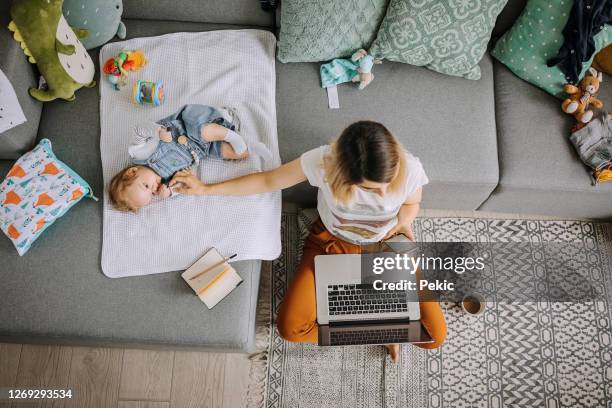 mutter arbeitet auf dem sofa mit dem laptop, während kleine kleine junge neben ihr liegen - multitasking stock-fotos und bilder