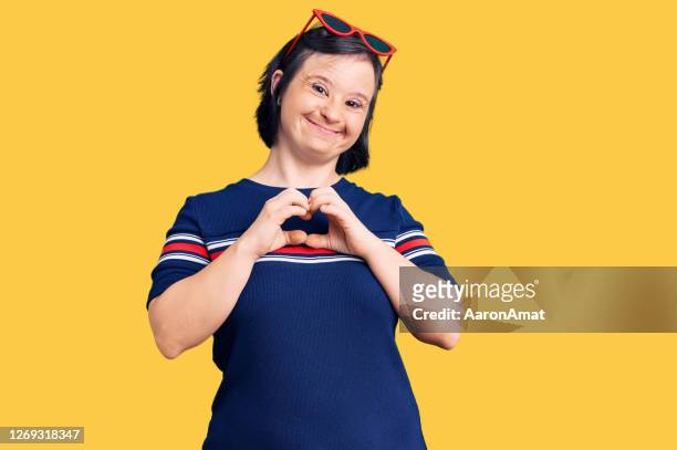 Brunette woman with down syndrome wearing casual clothes smiling in love showing heart symbol and shape with hands. romantic concept.