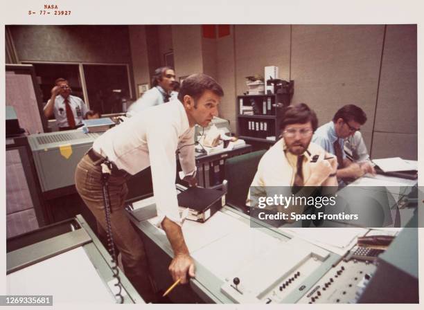 American NASA astronaut Joe Engle, stands leaning over the console, with other flight controllers to his left, monitors the activity in the mission...