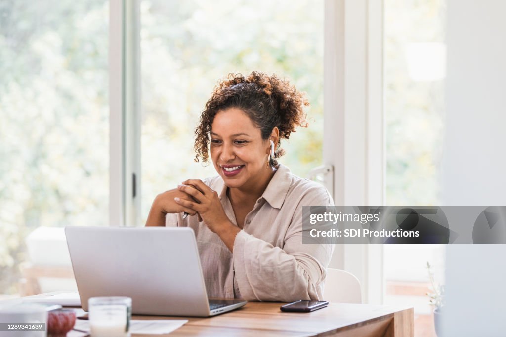 Using laptop and bluetooth earbuds, woman video conferences from home