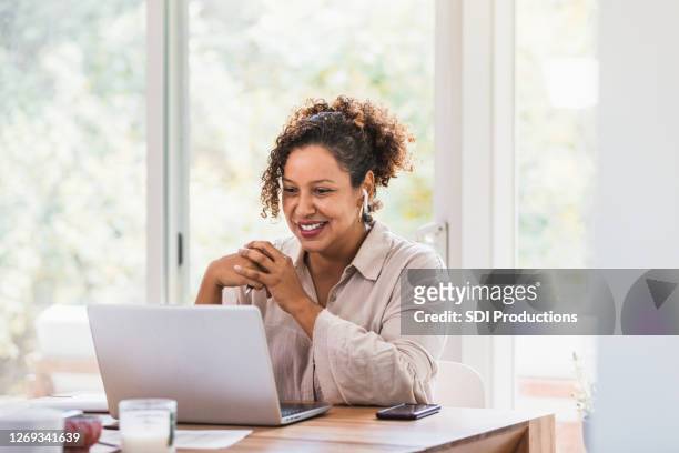 using laptop and bluetooth earbuds, woman video conferences from home - one person stock pictures, royalty-free photos & images