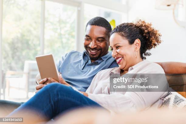 husband and wife enjoy using digital tablet during coronavirus lockdown - mid wife stock pictures, royalty-free photos & images