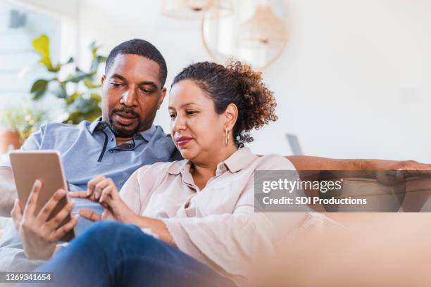 sheltering in place because of covid-19, the couple watches video - mid adult stock pictures, royalty-free photos & images