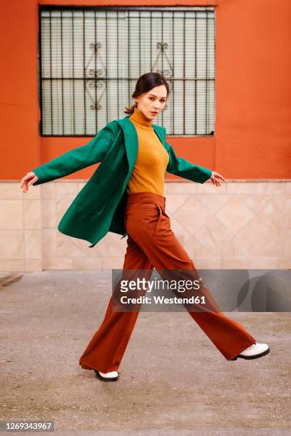 young woman wearing green jacket walking on footpath against building in city - fashion stock-fotos und bilder