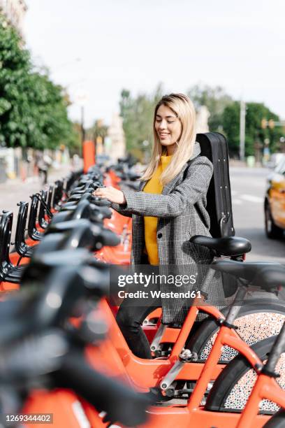 young woman with violin case renting bicycle in city - sustainable transportation stock pictures, royalty-free photos & images