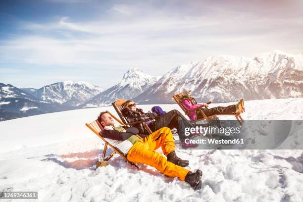 friends sunbathing in deck chairs in mountainscape in winter, achenkirch, austria - sunbathing stock pictures, royalty-free photos & images