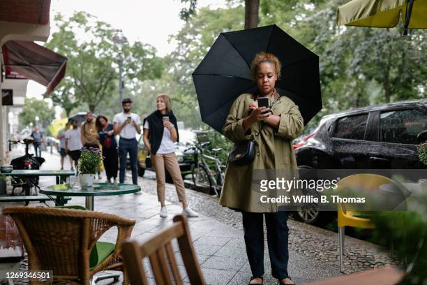 customers queuing for restaurant while social distancing - white and black women and umbrella stockfoto's en -beelden
