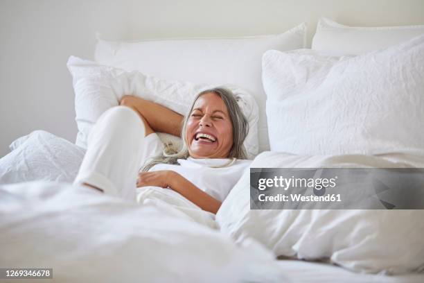 cheerful woman lying on bed at home - comfortable bed stock pictures, royalty-free photos & images