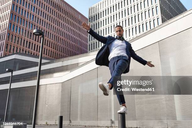 businessman with headphones balancing on pole against office building - pole positie fotografías e imágenes de stock