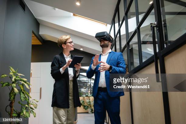 businesswoman analyzing colleague using virtual simulation headset in creative office corridor - casques réalité virtuelle photos et images de collection