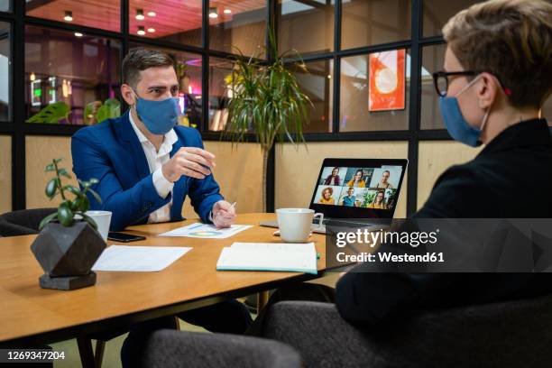male and female entrepreneurs wearing masks while planning strategy in board room during pandemic - zoom interview stock pictures, royalty-free photos & images