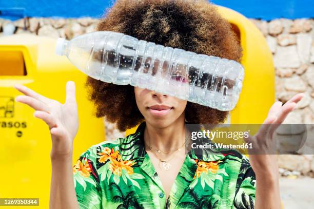 young woman throwing empty plastic bottle in front of recycling bin - gooien stockfoto's en -beelden