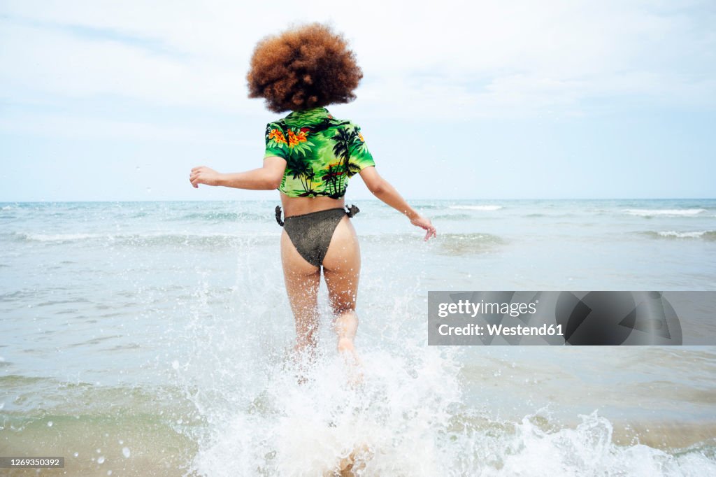 Rear view of young woman running at the beach