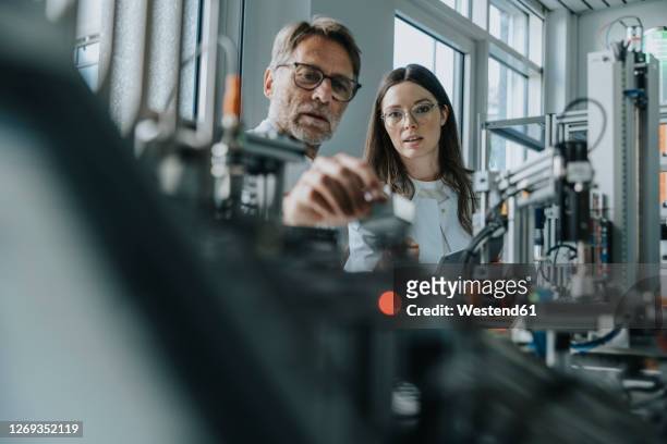 male scientist with young woman examining machinery in laboratory - herstellendes gewerbe stock-fotos und bilder
