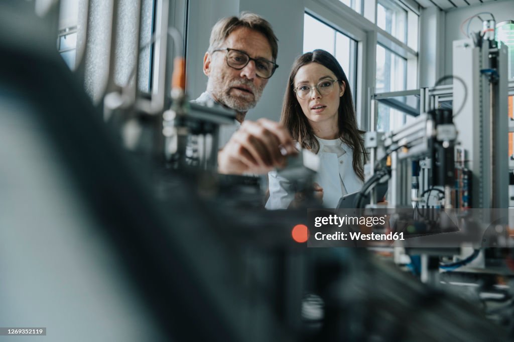 Male scientist with young woman examining machinery in laboratory