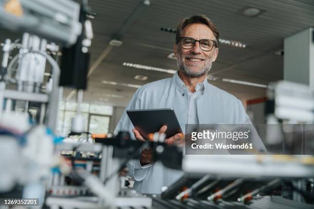smiling male scientist holding digital tablet while standing by machinery in laboratory - industrie porträt stock-fotos und bilder