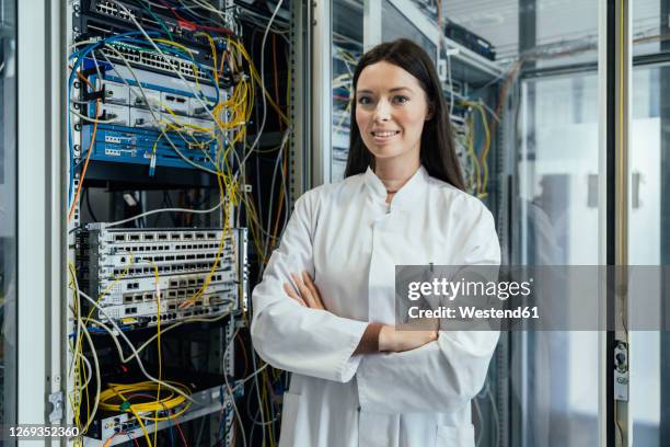 young woman with arms crossed standing in data center - fiber optics stock-fotos und bilder