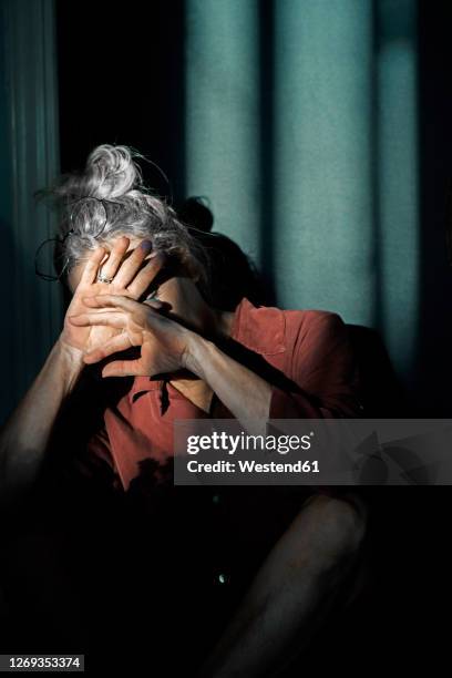senior woman shielding eyes while sitting against wall at home - shielding eyes stock pictures, royalty-free photos & images