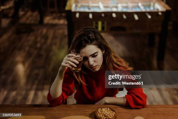 sad woman holding beer glass while sitting at table in restaurant - rubbing alcohol stock-fotos und bilder