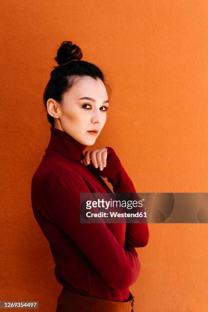 young woman wearing turtleneck long-sleeved top against orange wall - 長袖 ストックフォトと画像