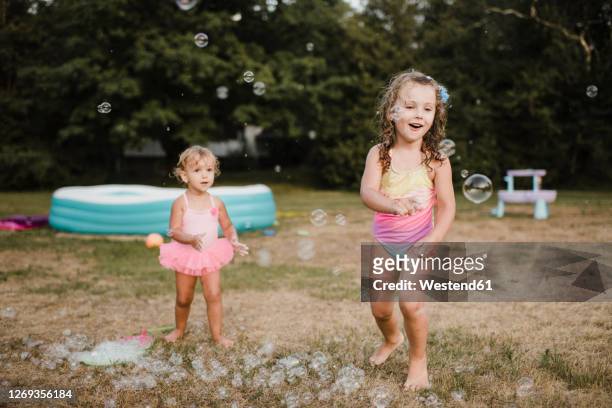 two happy girls playing with soap bubbles in garden - bubbles happy stockfoto's en -beelden