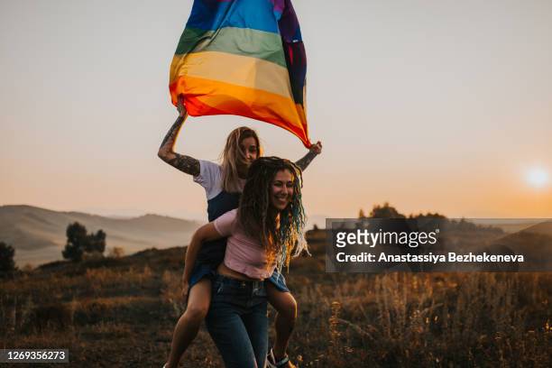two young laughing happy woman couple hugging - gay flag stock-fotos und bilder