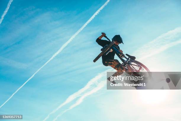 carefree man jumping while performing stunt with bicycle against blue sky during sunset - スタントバイク ストックフォトと画像