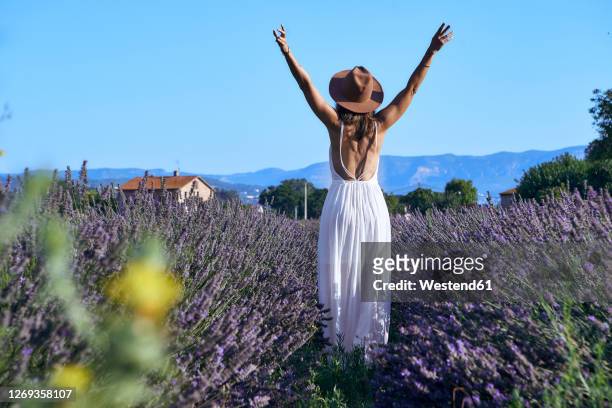 woman wearing white dress with arms raised standing amidst lavender field against clear sky - decollete photos et images de collection