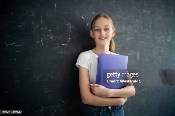 girl with exersice books in front of black wall - schulheft stock-fotos und bilder
