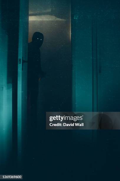 a halloween concept of a blurred scary, hooded figure, with glowing eyes. standing in a doorway. with a knife. with a vintage, abstract edit. - halloween scary stockfoto's en -beelden