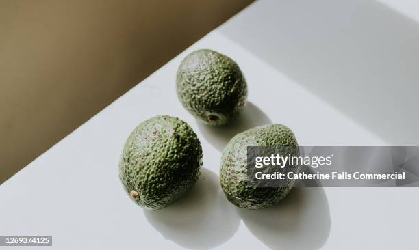 3 avocados on a white surface casting shadows - unripe stock pictures, royalty-free photos & images