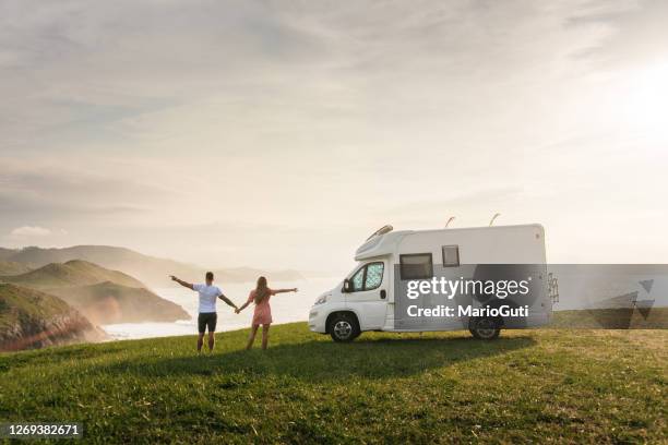 jong paar dat met hun motorhuis reist dat zich door het overzees met opgeheven wapens bevindt - couple on the beach with car stockfoto's en -beelden