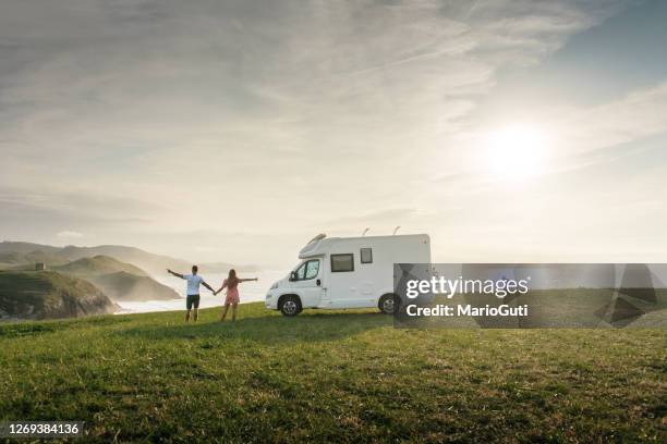 pareja joven que viaja con su autocaravana de pie junto al mar con los brazos levantados - trailer fotografías e imágenes de stock