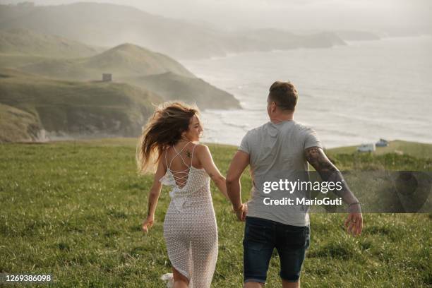 rear view of a carefree young couple running by the sea - young couple holding hands stock pictures, royalty-free photos & images